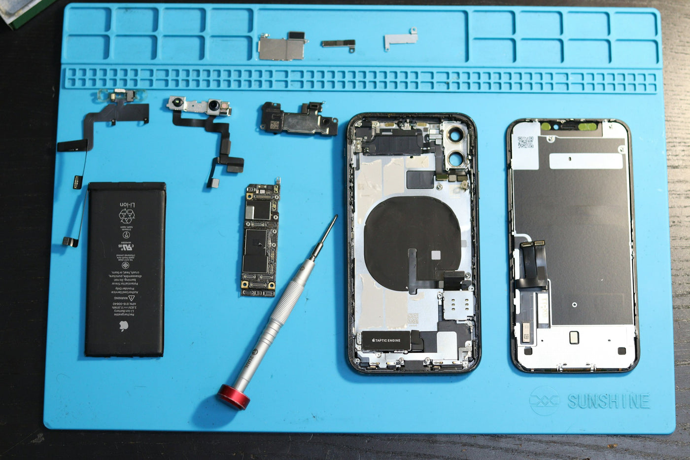 Zerlegtes iPhone mit Einzelteilen auf einer Reparaturmatte